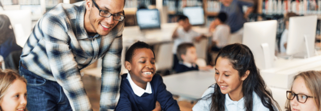 A practitioner leans over a table where 4 students sit. They are all smiling