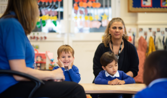 Child in classroom smiling with chin in hands