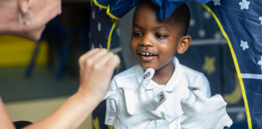 Child wearing gloves, smiling, looking at practitioner