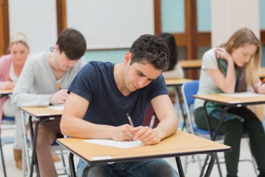 A level student sitting in exam room, working on exam paper. 