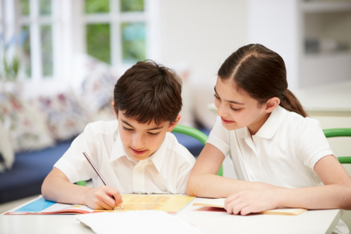 Two pupils in classroom, working together at desk, looking at paper on table.